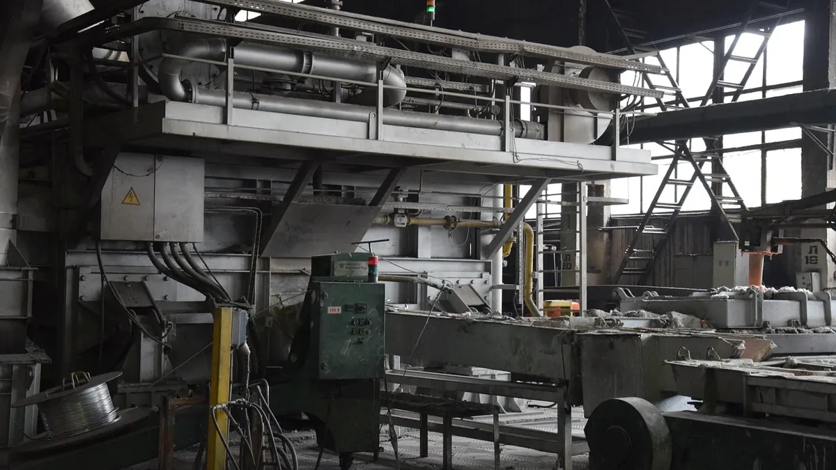 A large industrial machine with metal components, pipes, and a control panel, situated in a factory or warehouse setting.