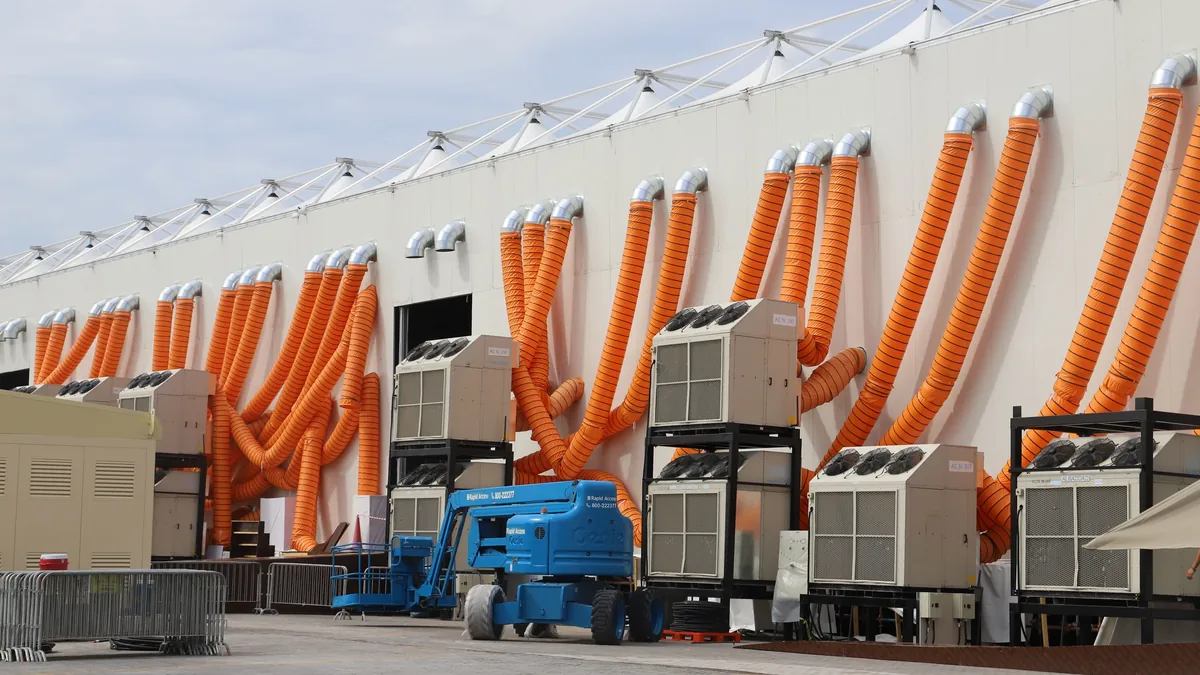 A large white building with multiple air conditioning units and orange hoses attached to them, situated in an industrial setting.