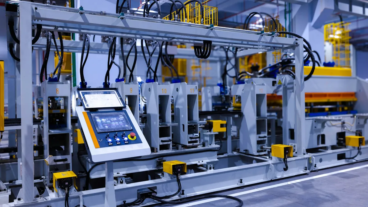 A large industrial machine with a control panel and various wires and cables attached to it, situated in a factory setting.