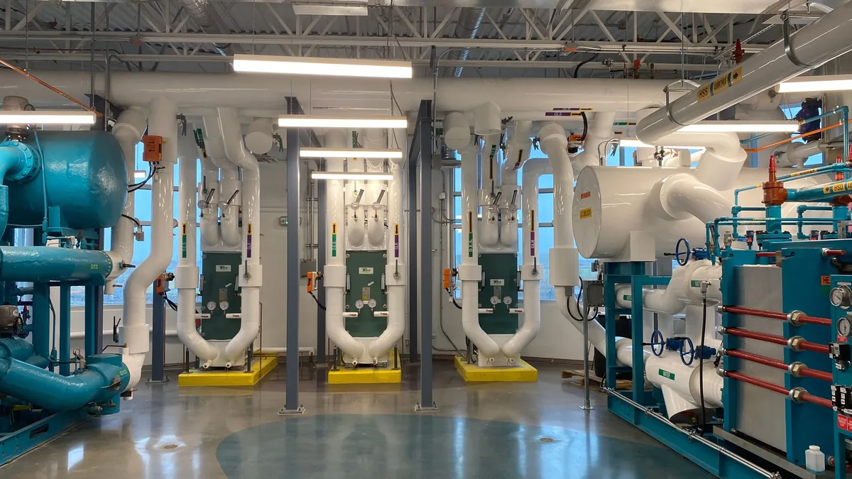 A large room with a polished concrete floor, featuring several large pieces of industrial equipment, including pipes, pumps, and control pan