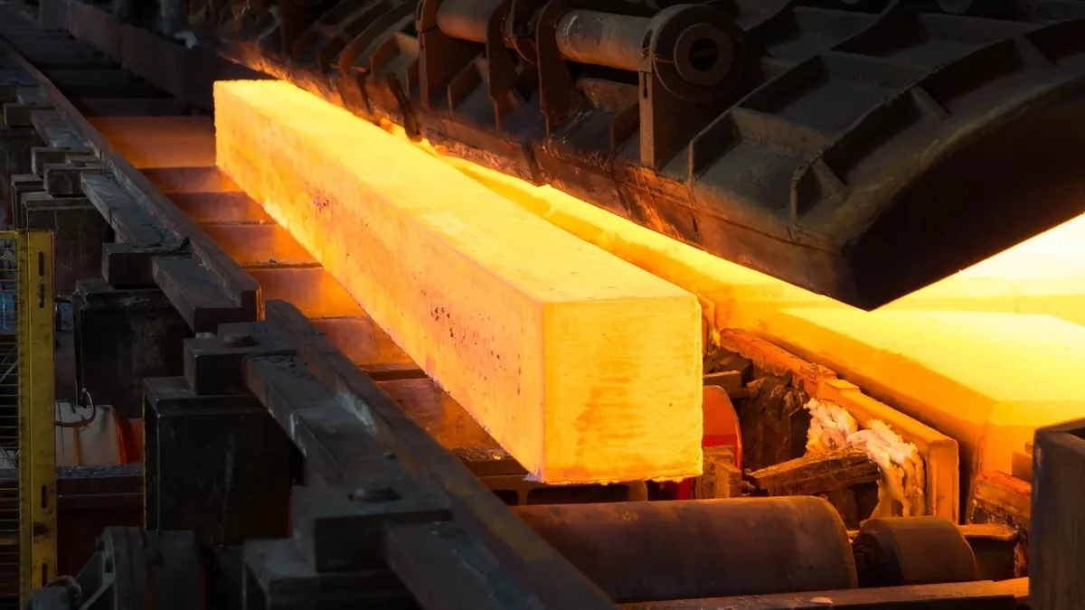 A large block of molten metal being transported on a conveyor belt in a factory setting.