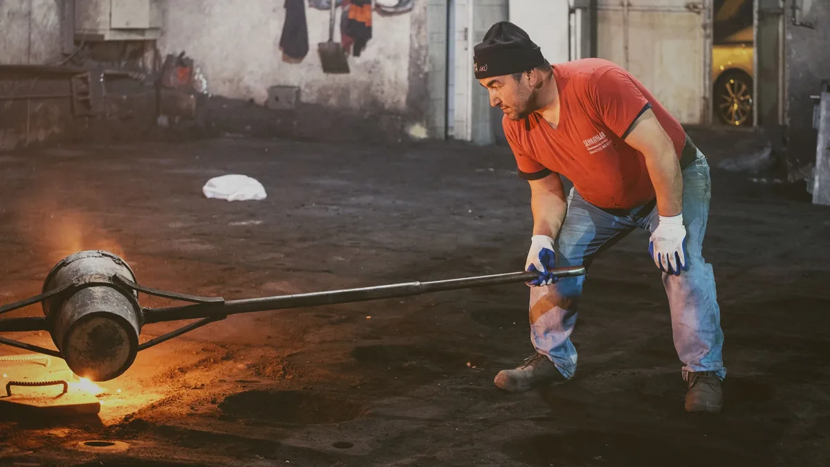A man is shown pouring molten metal from a crucible into a mold, with the metal glowing orange and emitting sparks as it flows.