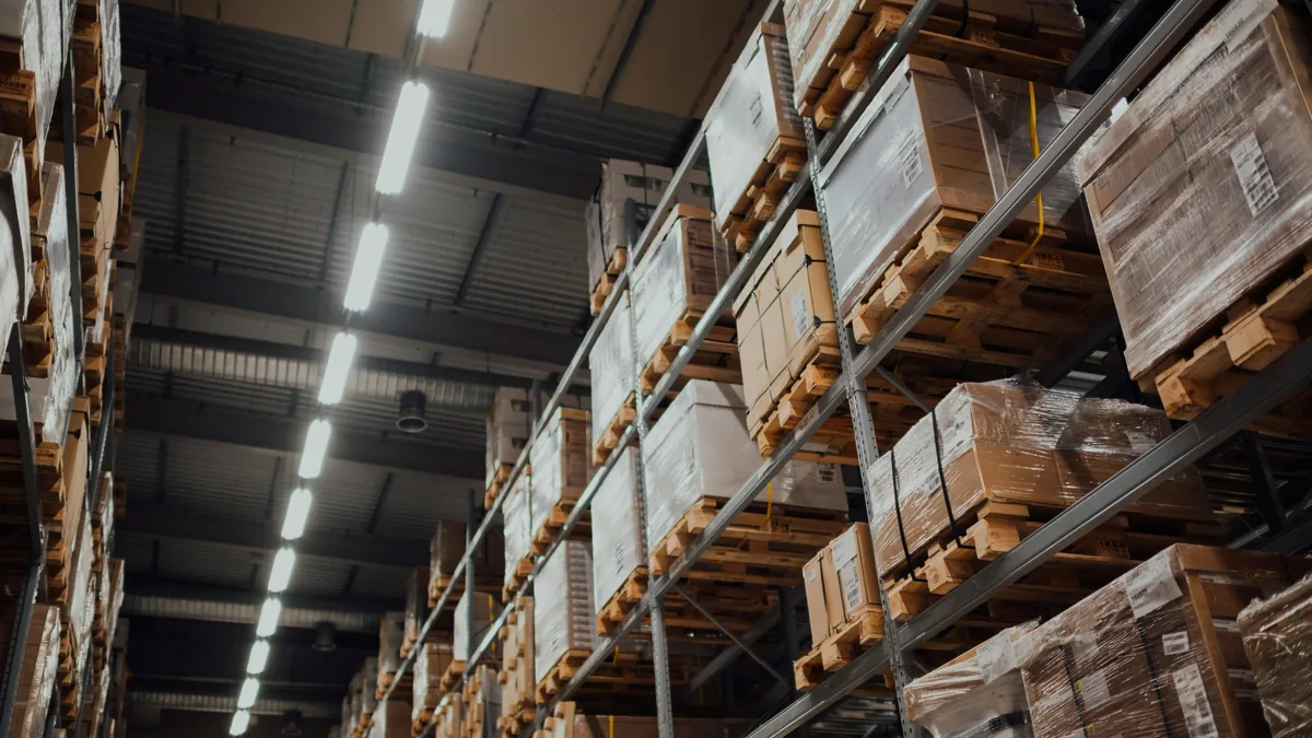 A warehouse with rows of shelving units stacked with wooden pallets containing cardboard boxes.