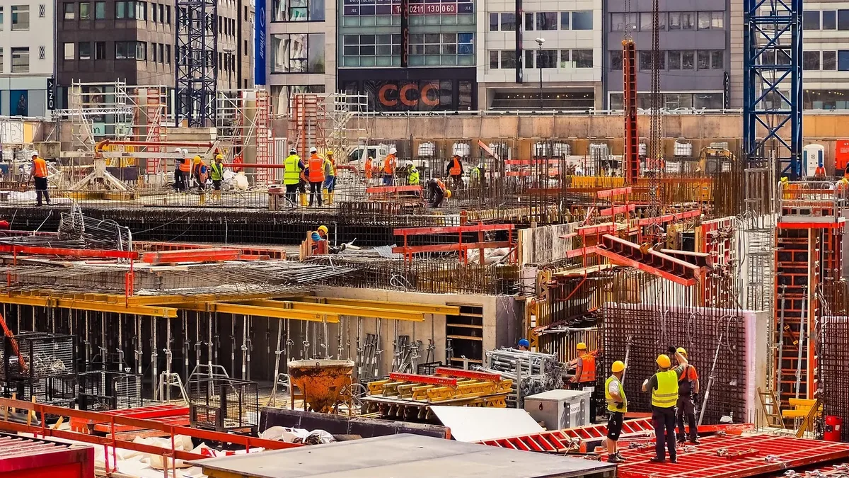 A construction site with workers in high-visibility clothing and hard hats, surrounded by scaffolding and building materials.