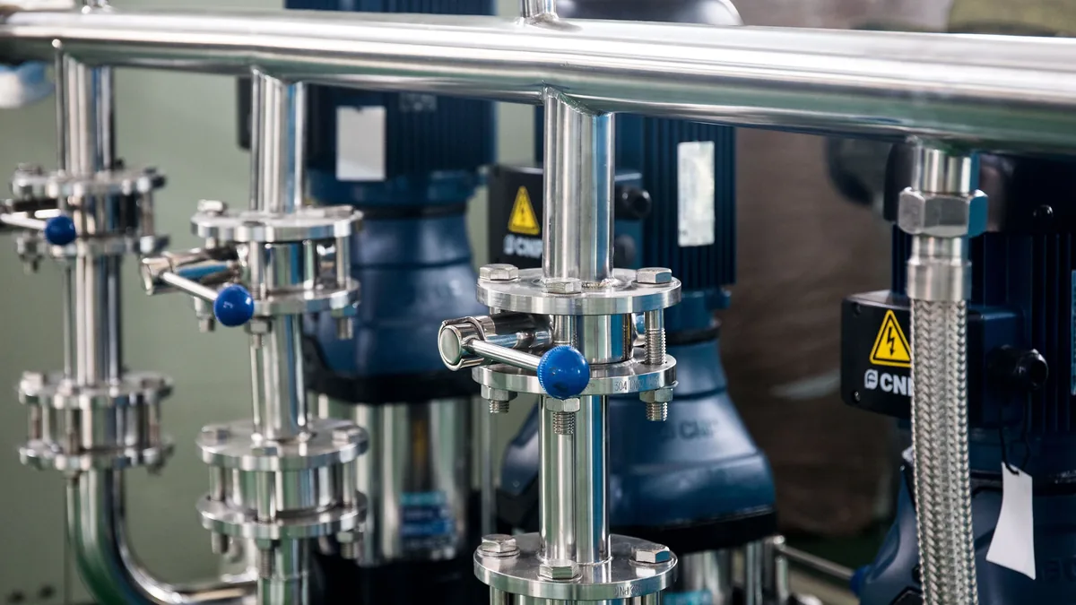 A close-up view of a metal pipe system with valves and pumps, likely in an industrial or manufacturing setting.