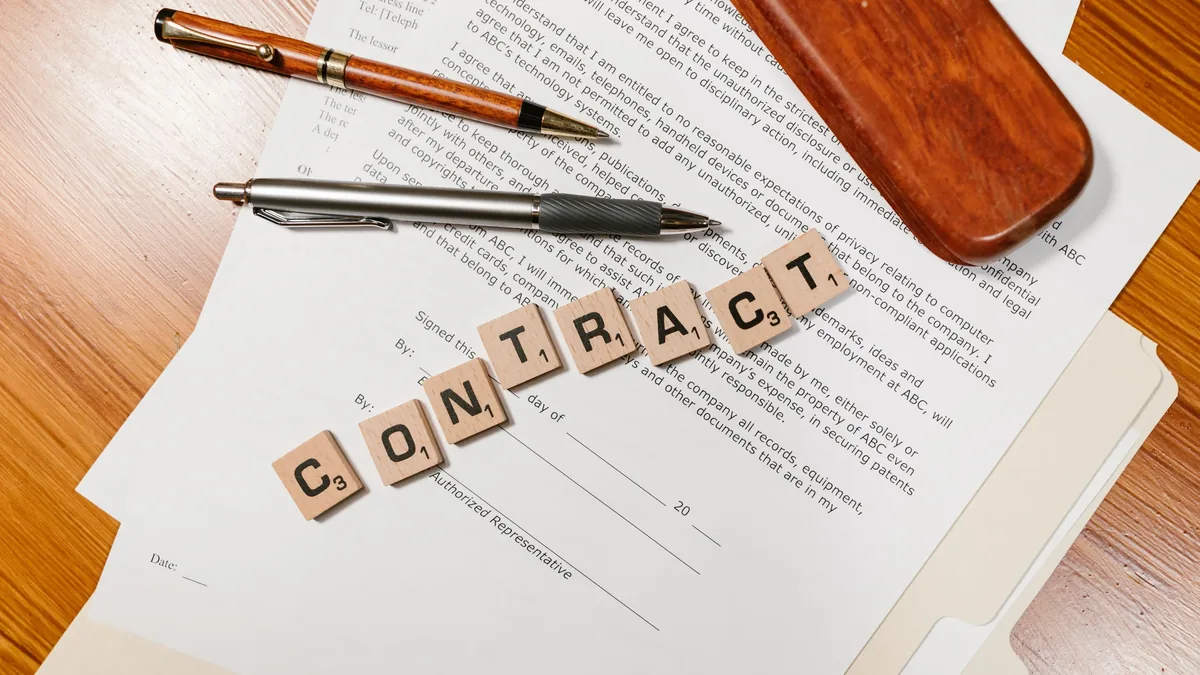 A contract, a pen, a pencil, and a wooden desk.